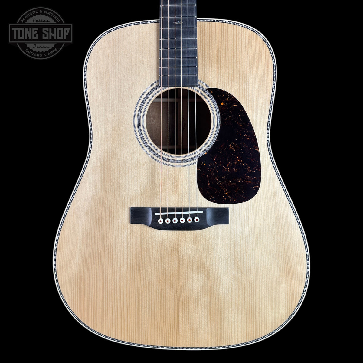 A close-up studio shot of an acoustic guitar body against a solid black background, featuring a natural wood finish, a dark tortoiseshell pickguard, and a black bridge. A circular 'TONE SHOP' watermark is visible in the top left corner.