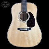 A close-up studio shot of an acoustic guitar body against a solid black background, featuring a natural wood finish, a dark tortoiseshell pickguard, and a black bridge. A circular 'TONE SHOP' watermark is visible in the top left corner.
