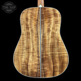 The back of an acoustic guitar made from a figured wood species with dramatic grain patterns, featuring a white binding edge and a neck visible at the top, set against a solid black background with a Tone Shop watermark in the upper left.