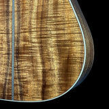 Close-up of a guitar body corner showing a rich, figured wood grain pattern in warm brown and golden tones, with a light-colored binding edge against a solid black background.