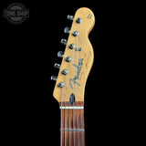 Close-up of a Fender Stratocaster electric guitar headstock in natural maple wood, featuring six silver tuning pegs and a dark brown fretboard, shown against a solid black background.