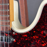 Close-up detail of an electric guitar showing the glossy red and black marbled tortoiseshell body, cream-colored body contour, and part of the dark wood fretboard.
