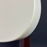 Close-up of a white circular product, showing a worn or chipped edge, with a dark navy background and a reddish-brown support visible below.
