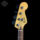 Close-up of a Fender Jazz Bass headstock made of natural maple wood, featuring four black cloud-shaped tuning pegs and silver tuning keys, set against a solid black background.