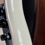 Close-up of a glossy cream-colored electric guitar body with black control knobs and a dark wood surface in the background.