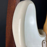 Close-up of the glossy cream-colored body of an electric guitar, showing the side contour and a portion of the light wood neck against a dark background.