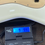 A close-up of a white electric guitar body resting on a black digital smart weigh scale with a blue LCD display showing 9.94 kg, set on a dark wooden surface.