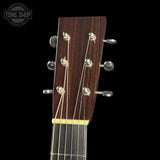 Close-up of a guitar headstock with tuning pegs on a black background, featuring the Tone Shop logo.