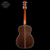 Back view of a wooden acoustic guitar on a black background with 'Tone Shop' logo.