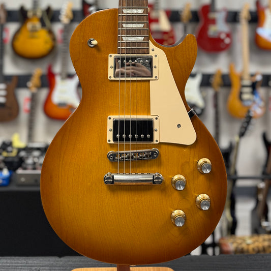 Close-up of a brown electric guitar on a stand with a blurred background of other guitars.