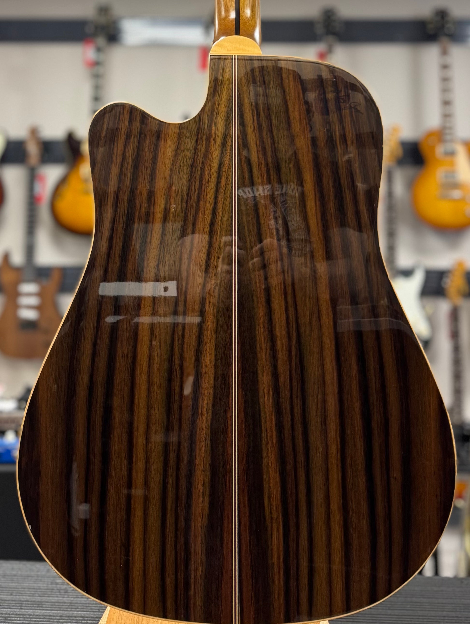 Close-up of a guitar's back with a wood grain pattern, blurred background of a music store.