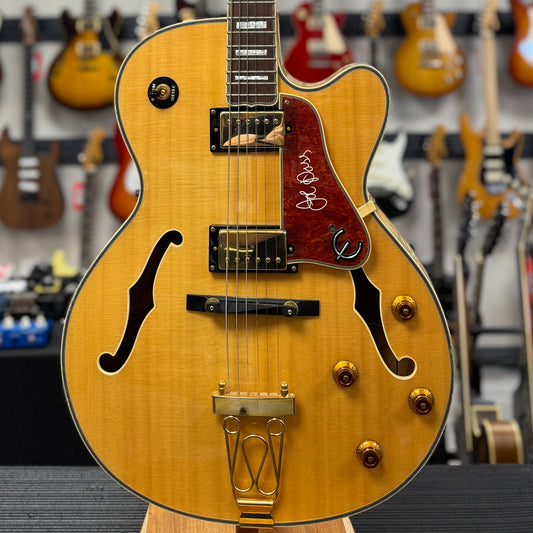 Close-up of a wooden electric guitar with a blurred background of other guitars.