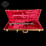 Red electric guitar in a red case with 'Tone Shop' logo.