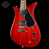Red electric guitar with a black pickguard on a black background, featuring the Tone Shop logo.