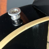 Close-up of a glossy black guitar body with a cream-colored binding edge and a silver metal tailpiece hardware piece.