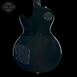 The back of a glossy black electric guitar, showing the body contour, pickups, and a clear cover over the lower bout control, set against a solid black background.