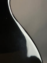 Close-up of a glossy black curved surface with a reflective white highlight against a dark gray background.