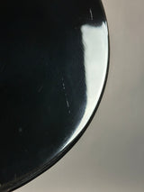 Close-up of a glossy black curved surface, likely part of a bowl, plate, or cup, with visible scratches and a bright reflection against a neutral gray background.