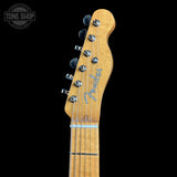 Close-up of a Fender electric guitar headstock in a natural maple finish, featuring six silver tuning pegs and the blue Fender script logo, set against a solid black background.