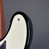 Close-up detail of an electric guitar body showing a glossy black edge trim and a silver screw on a cream-colored pickguard against a dark gray background.