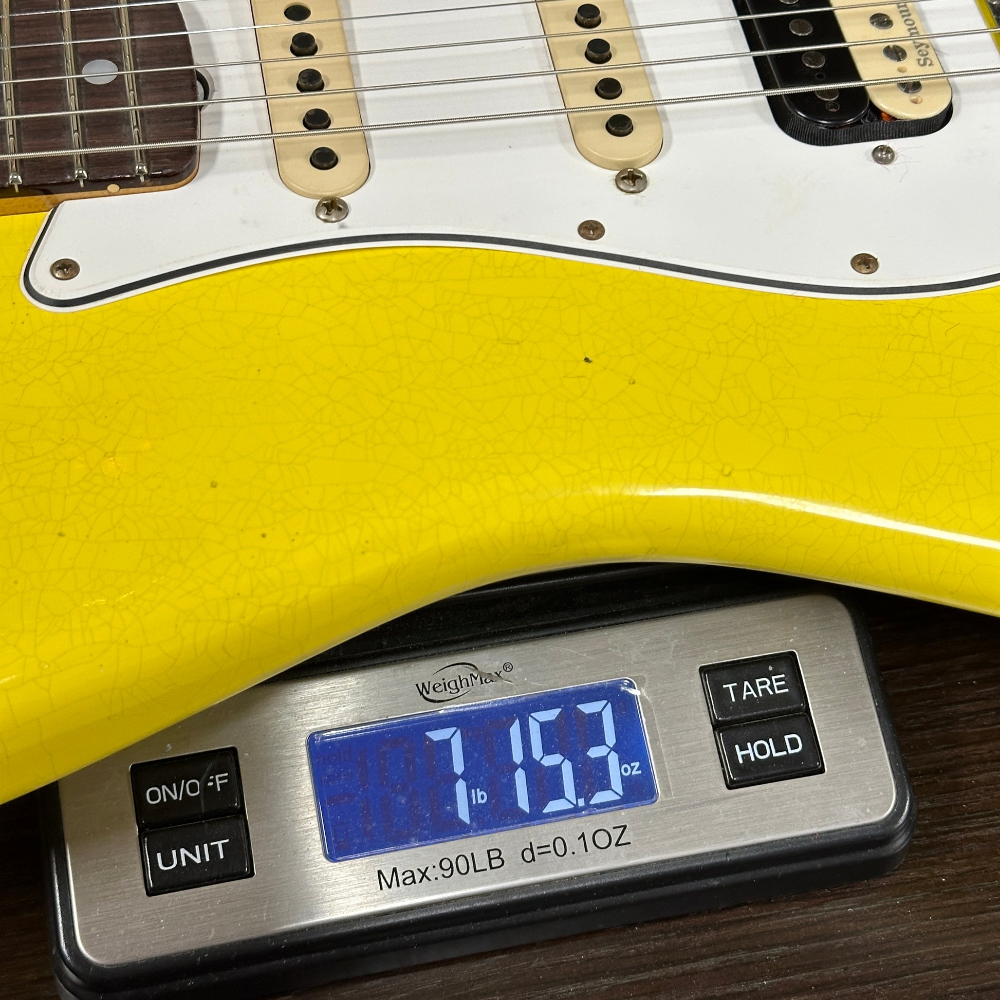 Yellow electric guitar on a digital scale displaying weight.