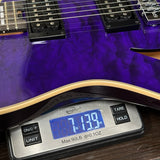 A close-up of a purple electric guitar body resting on a digital scale showing a weight of 7.139 lbs.