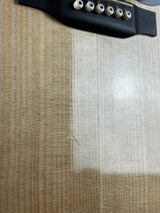 Close-up of a guitar's black bridge and six silver tuners resting on a light-colored wood-grain surface.