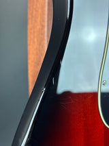 Close-up of a guitar with a red pickguard and wooden neck.