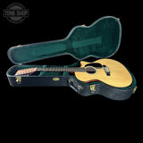 An acoustic guitar with a natural wood body and black pickguard resting inside an open dark green hard case, shown against a solid black background. A 'TONE SHOP' watermark is visible in the top-left corner.