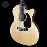 An acoustic guitar with a natural wood finish and dark brown sides, shown against a solid black background. A Tone Shop watermark is visible in the top-left corner.