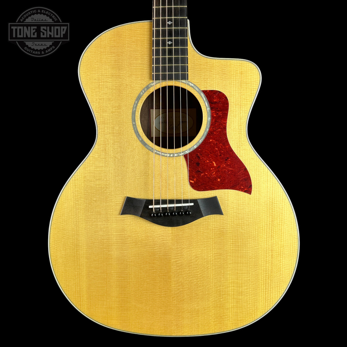 An acoustic guitar with a natural wood finish and a red glittery pickguard, shown against a solid black background with a Tone Shop watermark in the top left corner.