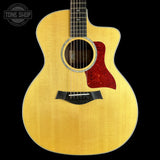 An acoustic guitar with a natural wood finish and a red glittery pickguard, shown against a solid black background with a Tone Shop watermark in the top left corner.