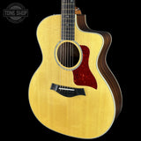 A Taylor acoustic-electric guitar with a natural wood top, dark wood sides, a red pickguard, and a cutaway body, shown against a black background with a Tone Shop watermark in the top left.