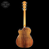 The back of an acoustic guitar with a rich, dark wood grain finish, shown against a solid black background with a Tone Shop watermark in the top-left corner.