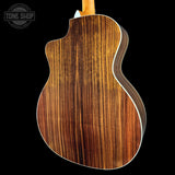 Close-up of the back of an acoustic-electric guitar showing a rich wood grain finish on a solid black background, with a Tone Shop watermark in the top left corner.