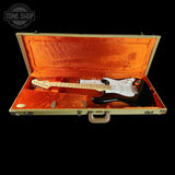 A Fender Stratocaster electric guitar with a white pickguard and black body, displayed inside an open vintage-style hard case with orange velvet lining, set against a solid black background.