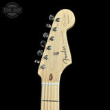 Close-up of a Fender Stratocaster electric guitar headstock in natural maple wood, featuring six silver tuning pegs and the Fender logo, set against a solid black background.