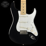 A black electric guitar with a white pickguard and maple neck, photographed against a solid black background. A Tone Shop watermark is visible in the top-left corner.