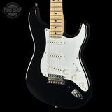 A black electric guitar with a white pickguard and maple neck, photographed against a solid black background. A 'TONE SHOP' watermark is visible in the top-left corner.