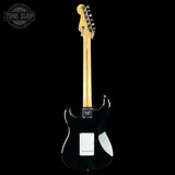 A black electric guitar shown from the back against a solid black background, featuring a light natural wood neck and a white pickguard.