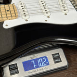 Close-up of a guitar body resting on a digital scale, with the scale displaying 7.102 oz.