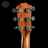 Close-up of the headstock of a guitar with a warm brown wood finish and six silver tuning pegs, set against a solid black background. A 'TONE SHOP' watermark is visible in the top-left corner.