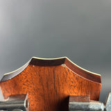 Close-up of the top edge of a wooden headstock, showing the wood grain and a small defect on the upper right side, with a dark gray background.