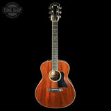 A Taylor acoustic guitar with a warm reddish-brown wood finish, shown vertically against a solid black background. The brand logo 'TAYLOR' is visible on the headstock, and a 'TONE SHOP' watermark is in the top-left corner.