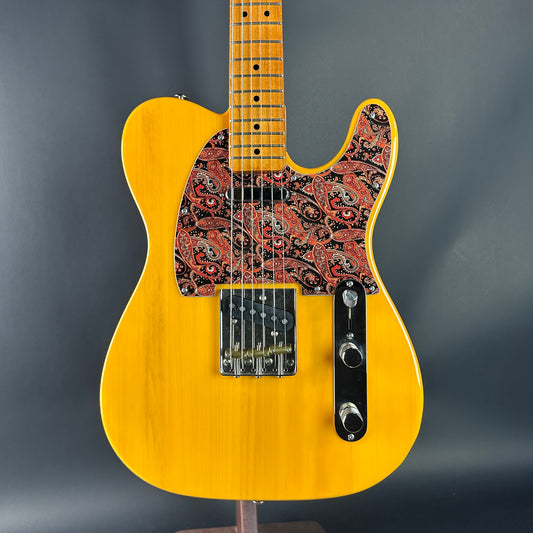 Yellow electric guitar with a patterned pickguard on a gray background