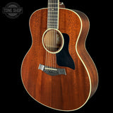 A close-up of an acoustic guitar body showing a rich reddish-brown wood grain finish, a black pickguard, and cream-colored binding, set against a solid black background with a Tone Shop watermark in the top-left corner.