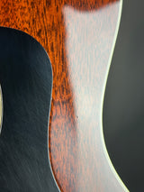 Close-up detail of an acoustic guitar body showing the glossy reddish-brown wood top, a dark black soundhole surround, and a light cream binding edge against a dark background.