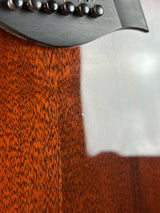 Close-up of a glossy reddish-brown wood surface with a dark metallic object partially visible on the left, showing a few reflective black spherical elements.