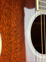 Close-up of an acoustic guitar body showing the glossy reddish-brown wood grain, the sound hole, and part of the fretboard with strings.