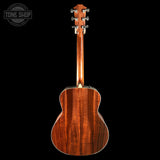 The back view of an acoustic guitar with a rich, warm brown wood grain finish, shown against a solid black background with a Tone Shop watermark in the top-left corner.